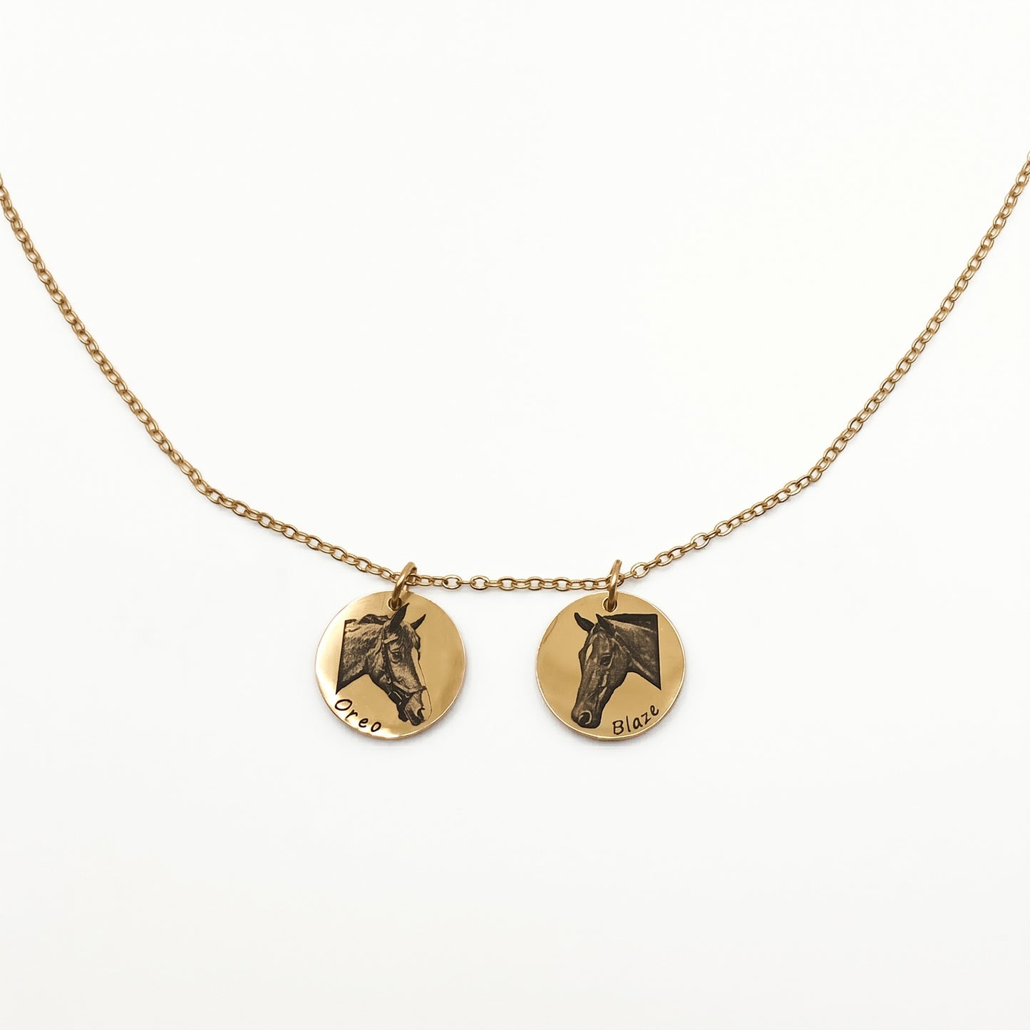 Gold necklace with two round pendants featuring horse faces on a white background