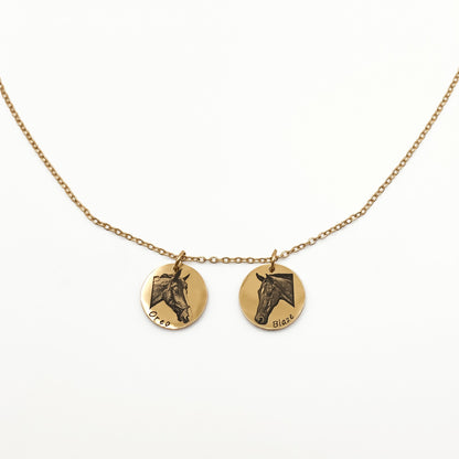 Gold necklace with two round pendants featuring horse faces on a white background