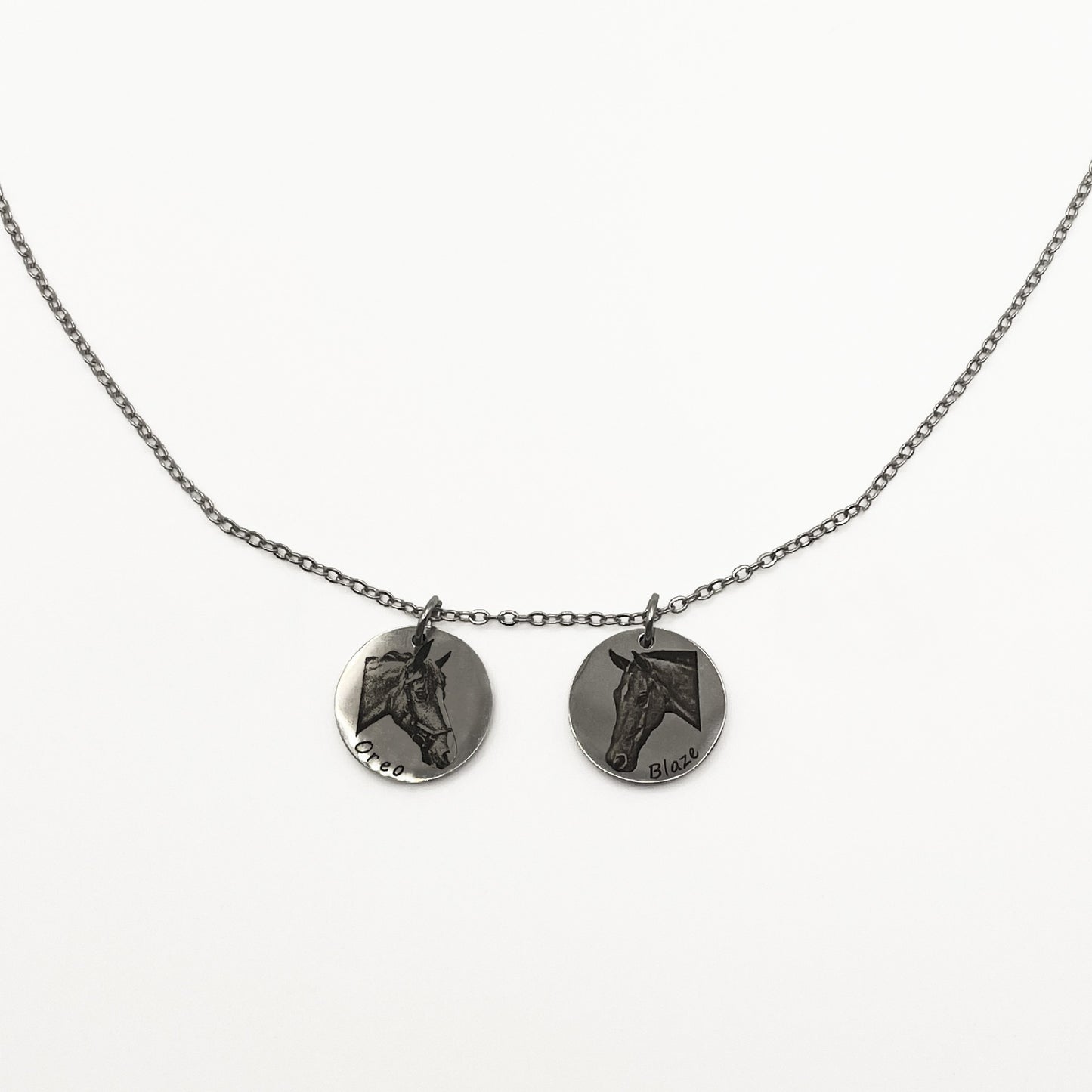Necklace with two circular silver pendants featuring engraved horse faces on a white background