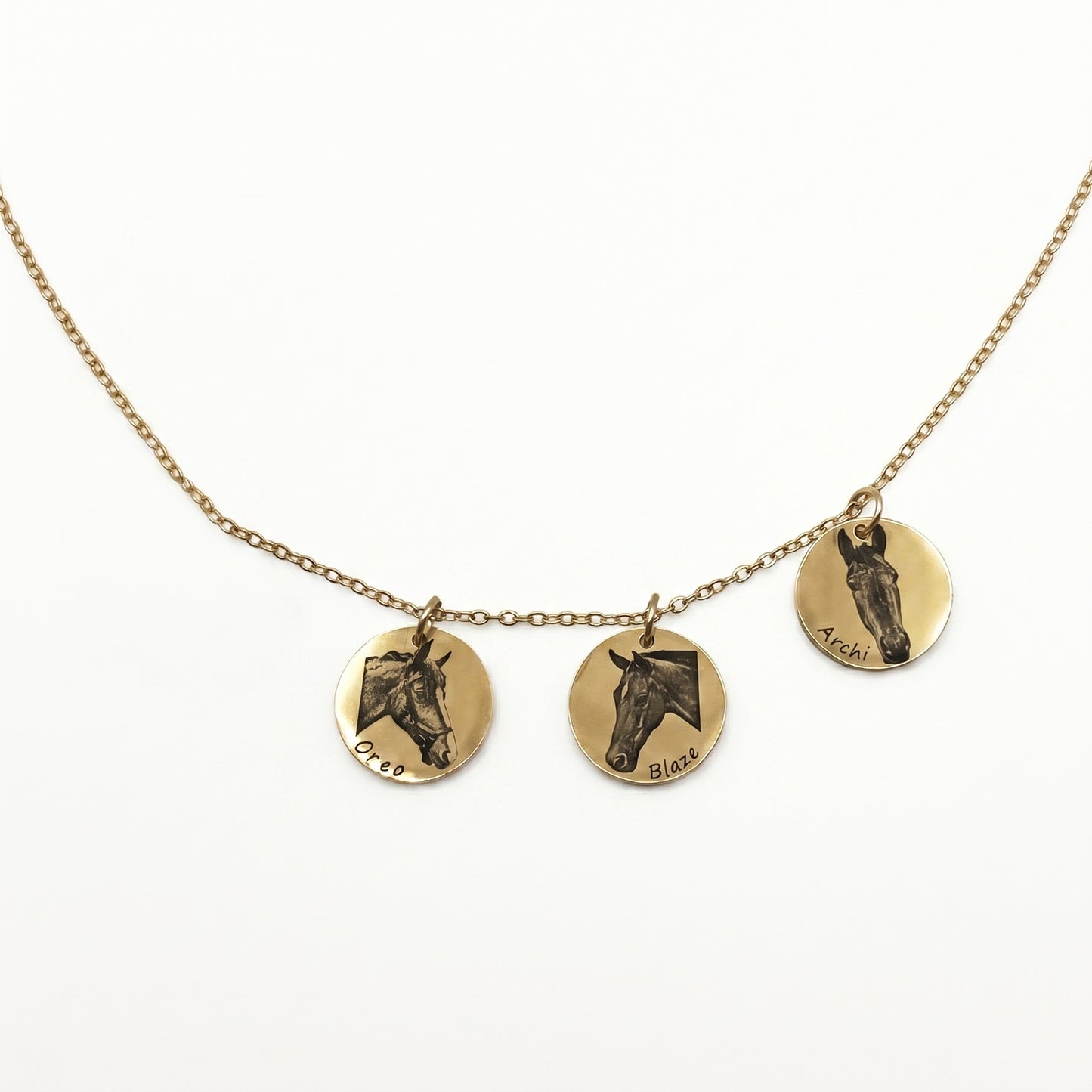 Necklace with three circular gold pendants featuring engraved horse faces on a white background