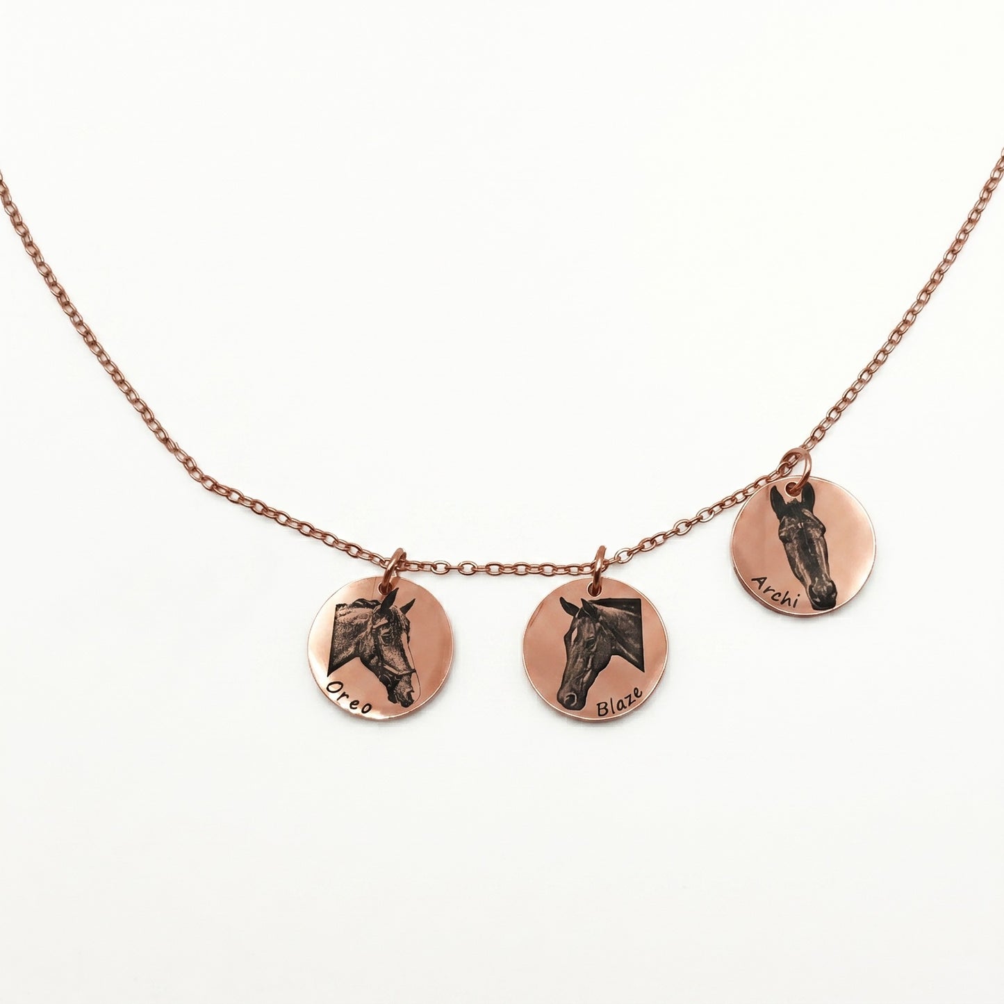 Necklace with three circular rose gold pendants featuring engraved horse faces on a white background