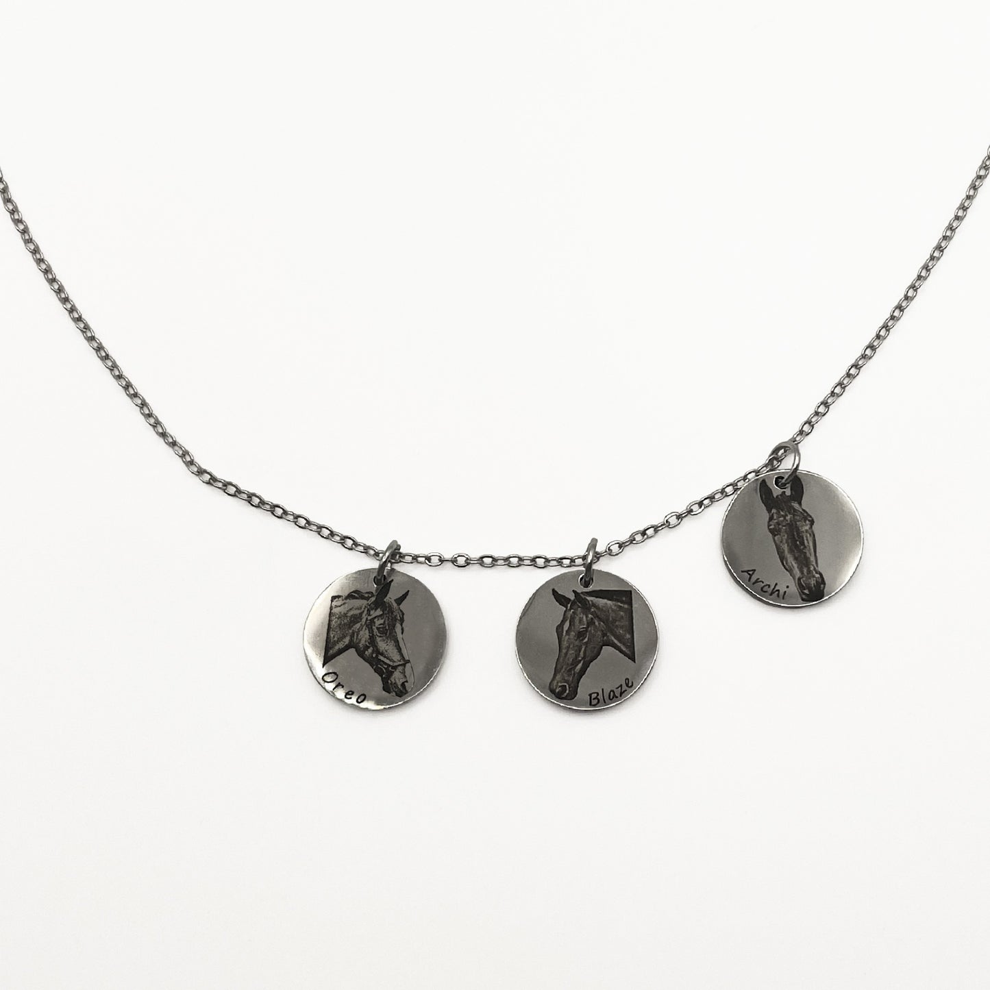 Necklace with three silver circular pendants featuring engraved horse faces on a white background